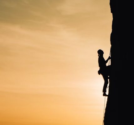 A silhouette of a rock climber scaling a steep cliff during sunset in Russia, showcasing determination and adventure.